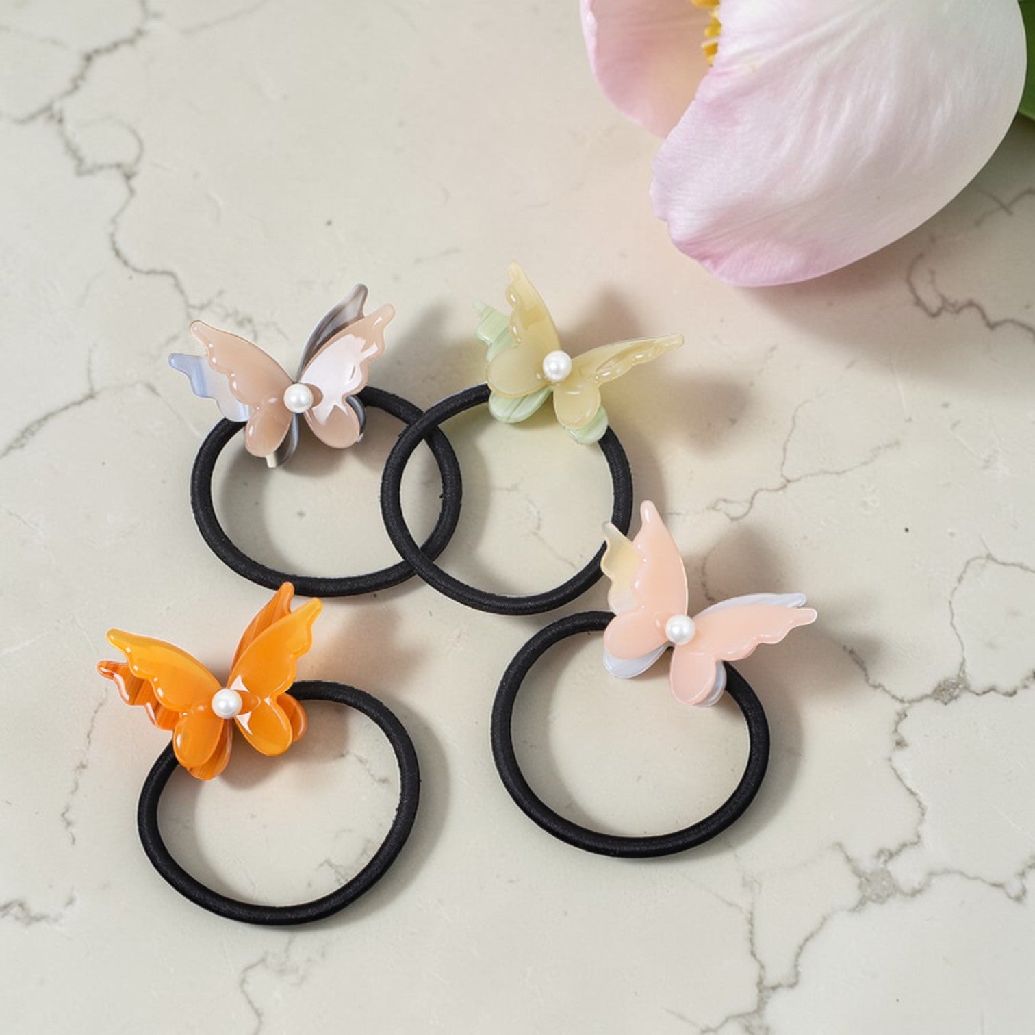 Set of butterfly-shaped hair ties on a marble surface with a pink flower.