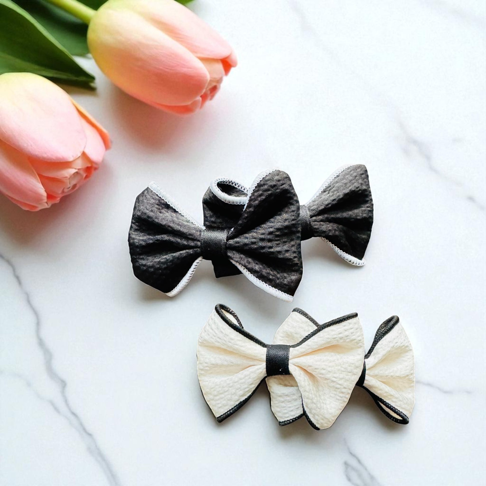 Two bow-shaped hair accessories on a white surface with pink tulips in the background.