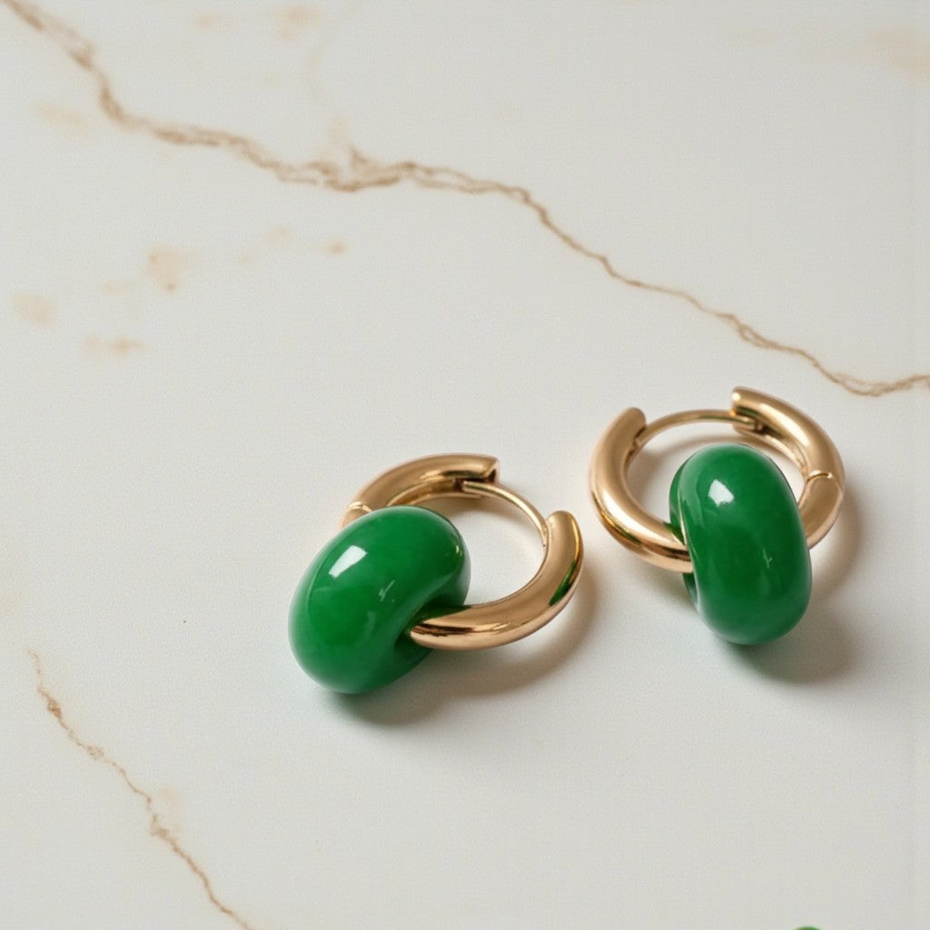 Gold hoop earrings with green stones on a marble surface