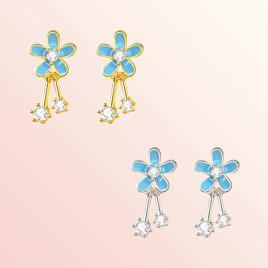 Flower-shaped earrings with blue petals and gold and silver accents on a light pink background