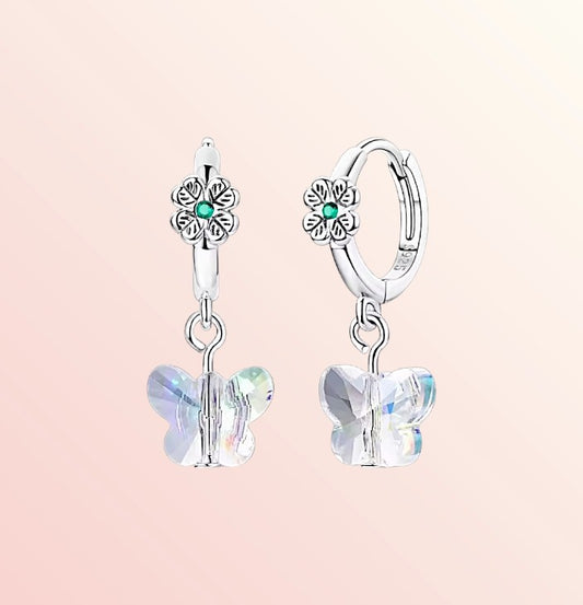 Silver earrings with butterfly charms on a light pink background