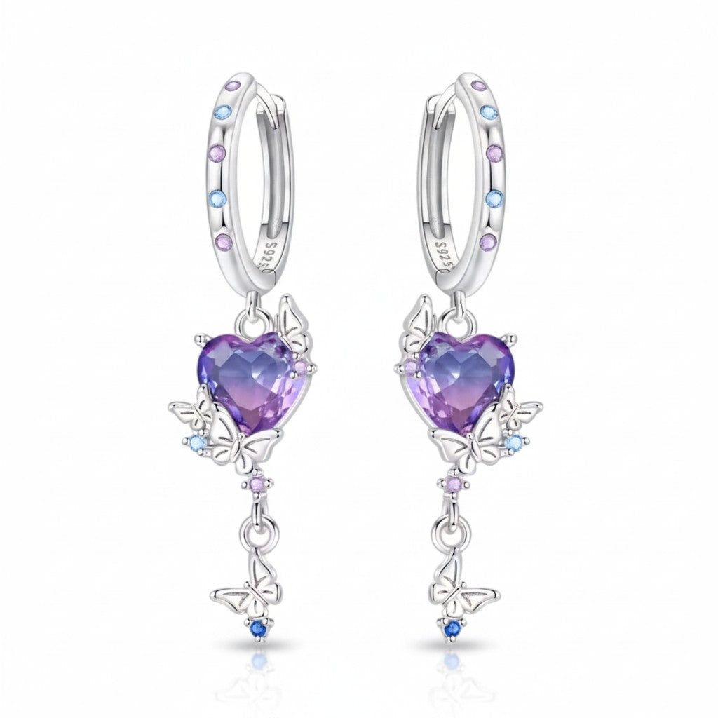 A pair of silver huggie hoop earrings with dangling heart-shaped purple gemstones, butterfly motifs, and small colorful accent stones, shown on a clean white background.