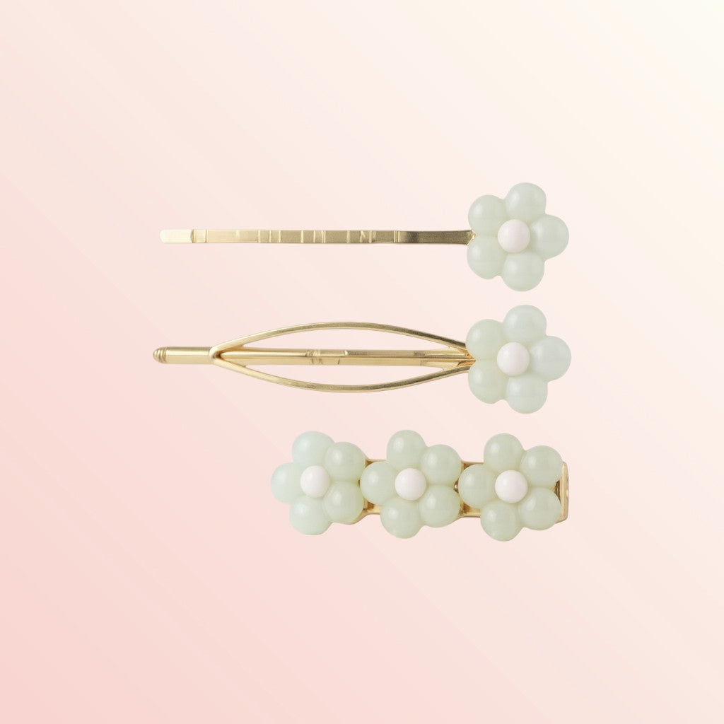 Set of three floral hair pins with gold accents on a light pink background