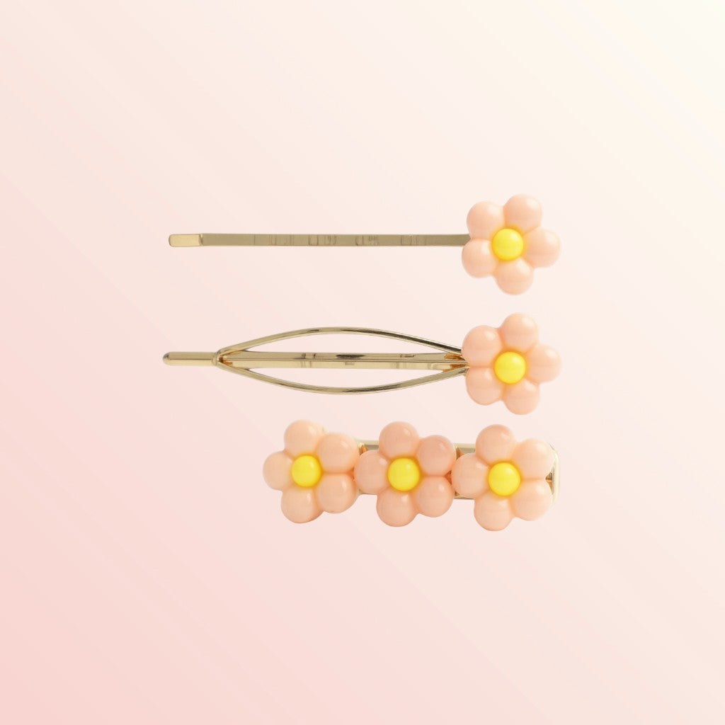 Set of three floral hair pins with yellow centers on a light pink background