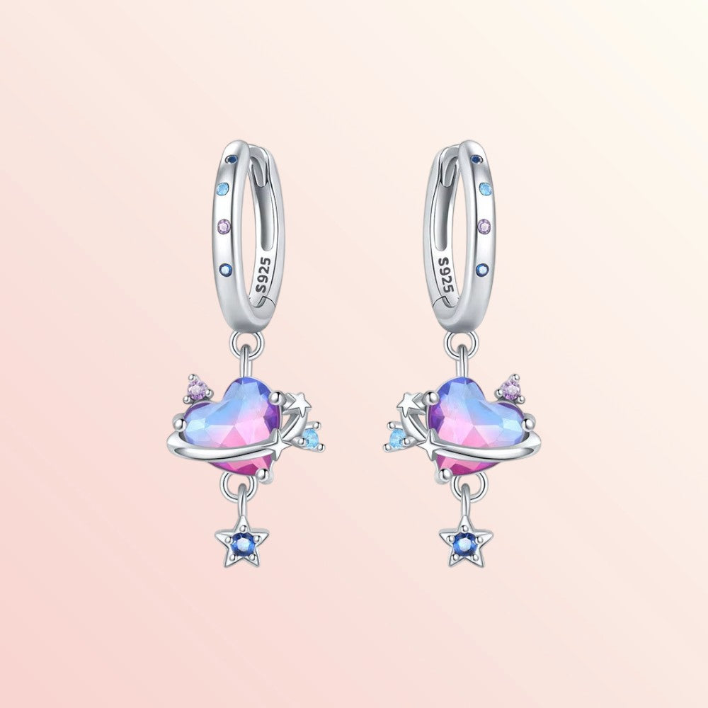 Pair of silver earrings with heart-shaped gemstones on a pink background