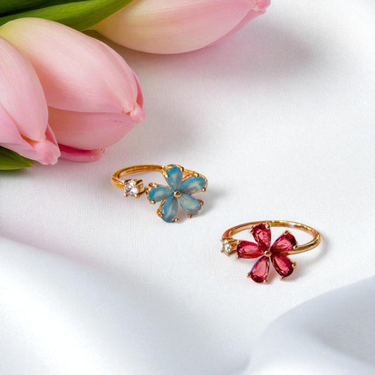 Two floral-themed rings with pink and blue gemstones on a white background with pink tulips.