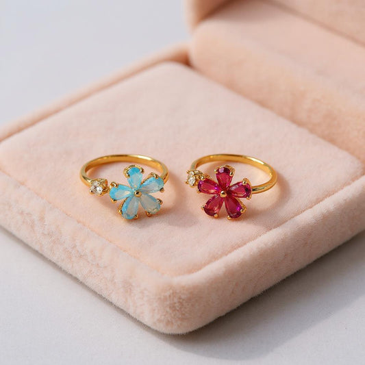 Two gold rings with gemstone designs on a pink cushion