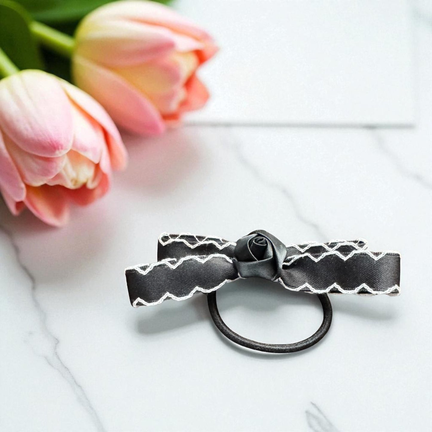 Black hair tie with white pattern on a white surface with pink tulips in the background