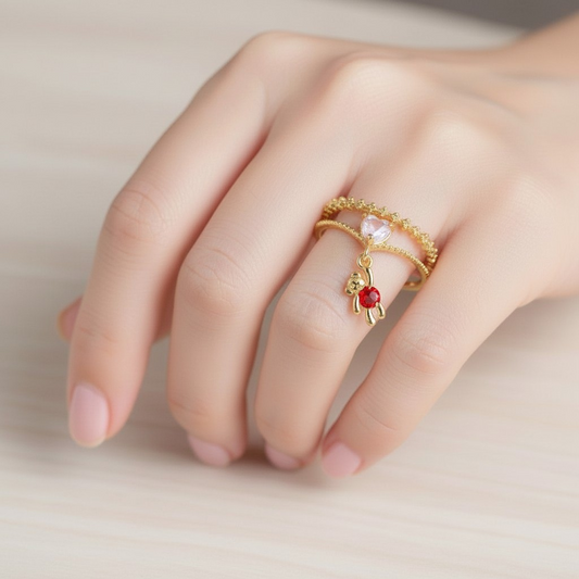 Close-up of a hand wearing a gold ring with a red gemstone on a neutral background