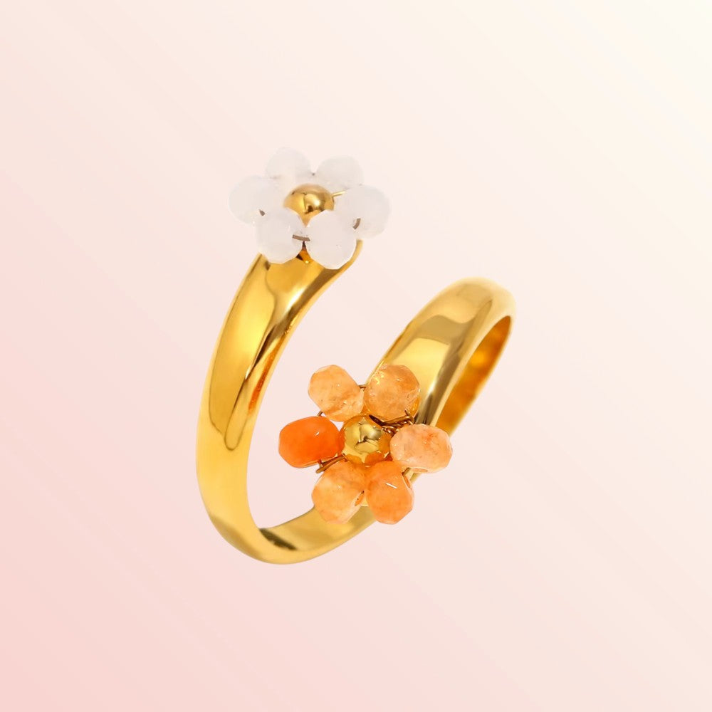 Gold ring with orange floral accents on a light pink background