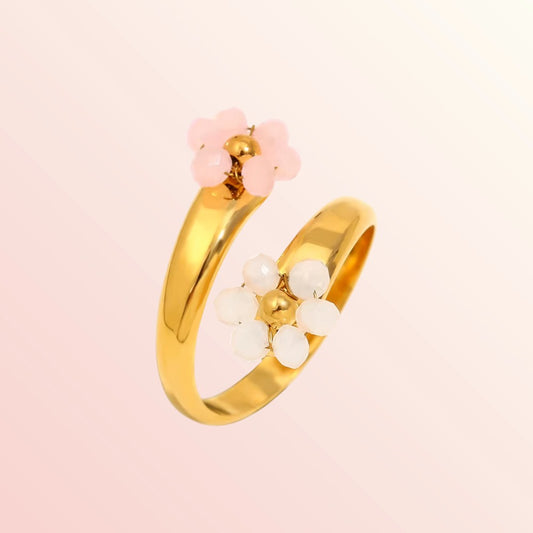 Gold ring with pink and white floral accents on a light pink background