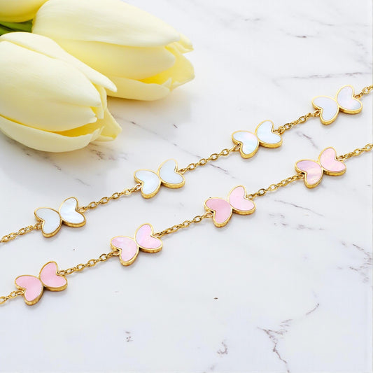 Butterfly-shaped necklace with pink and white wings on a marble surface with yellow tulips.