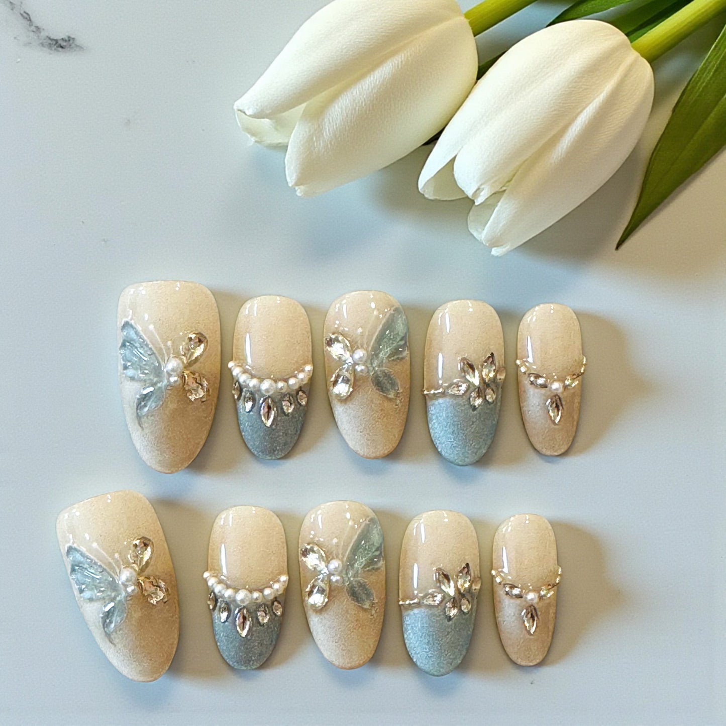 Decorative nail art with butterflies and pearls on a white surface with tulips in the background
