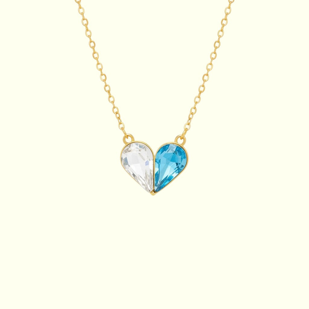 Heart-shaped necklace with one clear and one blue gem on a gold chain against a white background