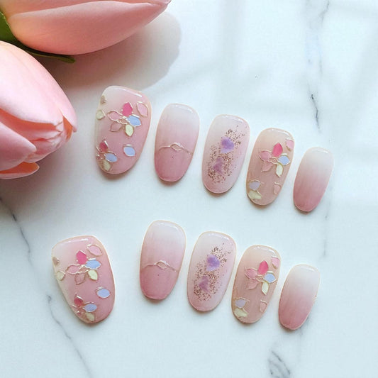 Pink nail art with floral designs on a marble surface with pink tulips.