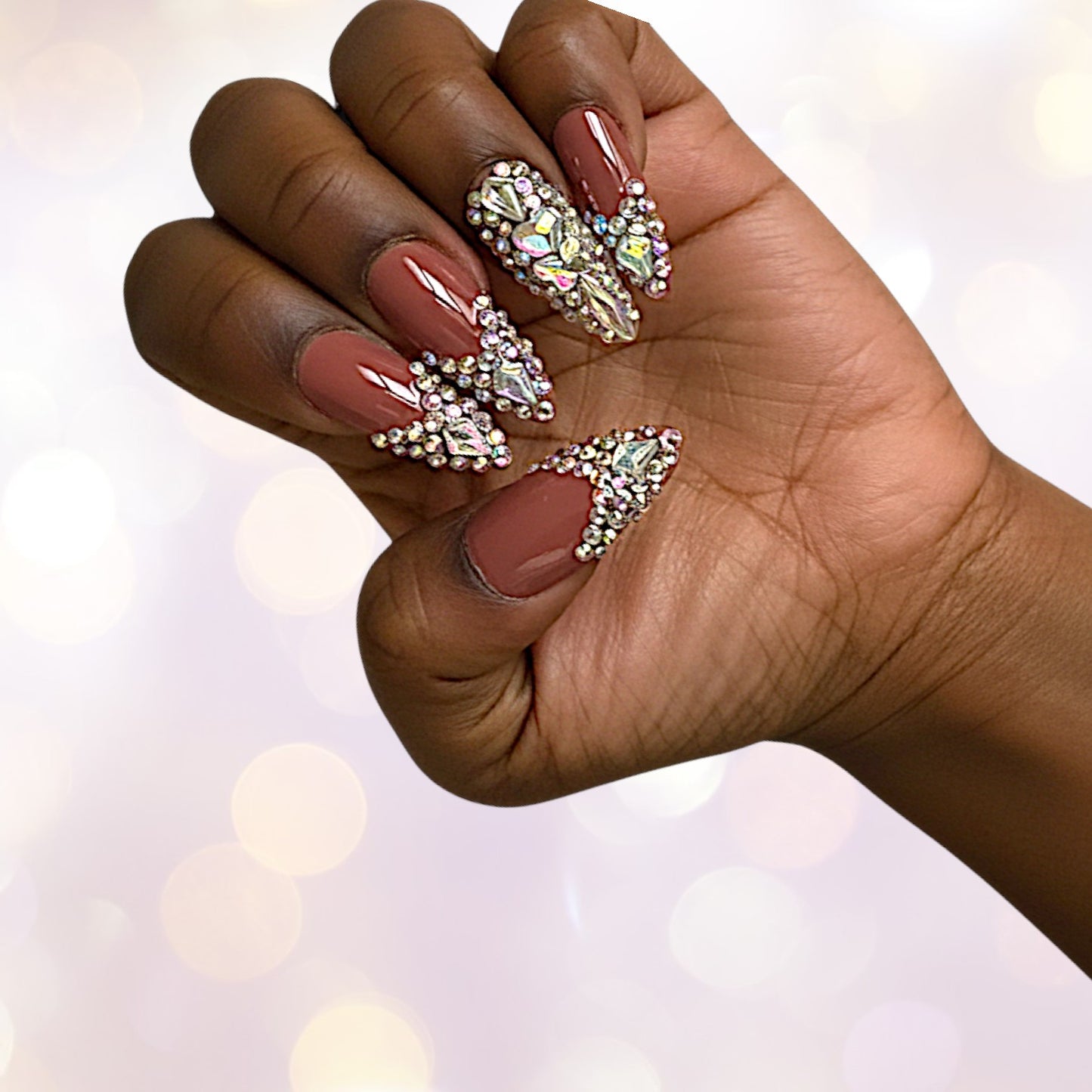 Hand with maroon nails featuring rhinestone designs against a blurred background