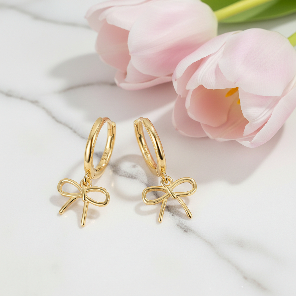 Gold bow-shaped earrings on a marble surface with pink tulips in the background