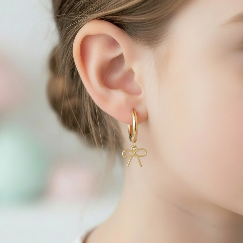 Gold hoop earring with a bow charm worn by a person.