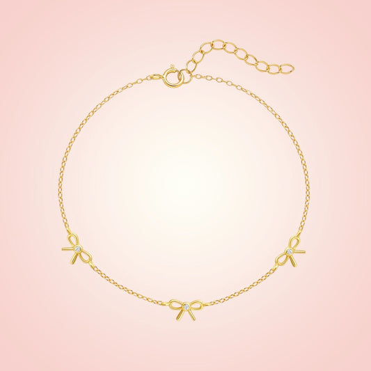 Gold bracelet with bow-shaped charms on a pink background