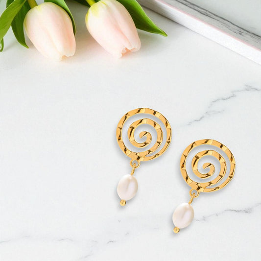 Gold spiral earrings with pearl drops on a marble surface with tulips.