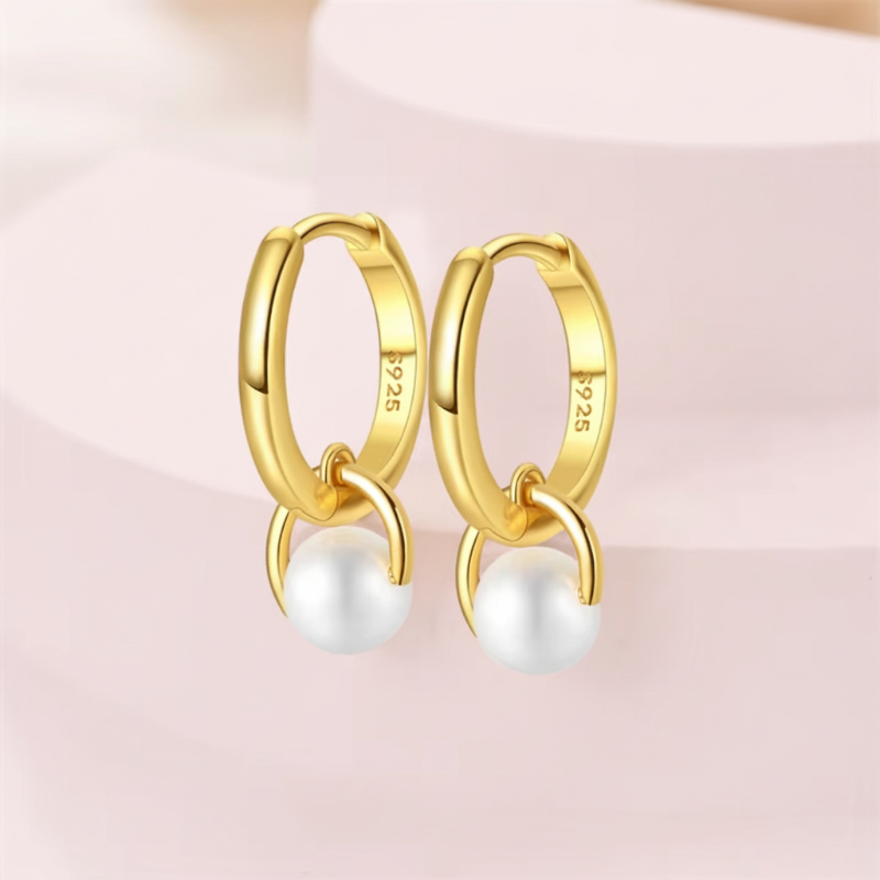 Gold hoop earrings with pearls on a light pink background