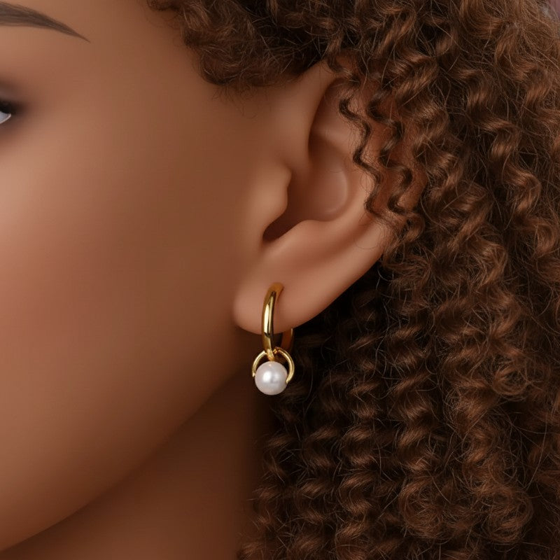 Close-up of an ear wearing a gold hoop earring with a pearl, against a blurred background.