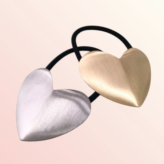 Heart-shaped hair ties in gold and silver on a light pink background