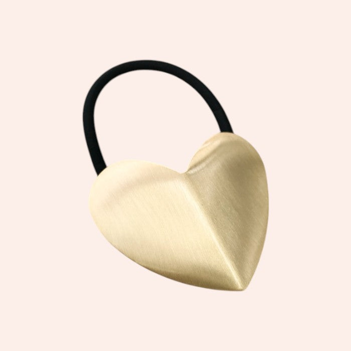 Heart-shaped brass hair tie on a light pink background