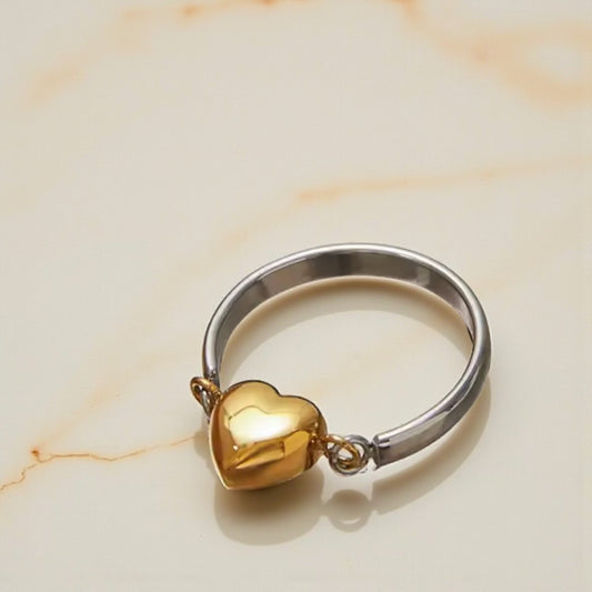 Gold heart-shaped charm on a silver ring against a beige marble background