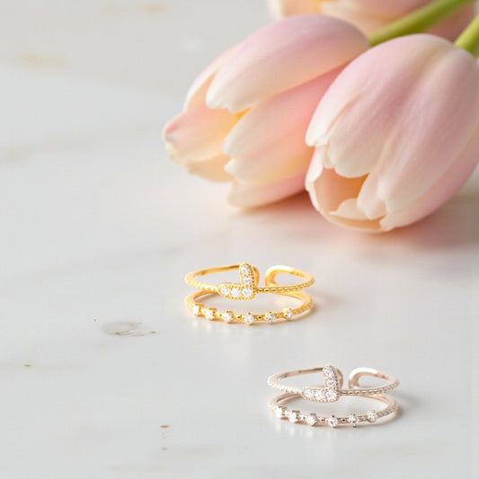 Two gold rings on a light surface with pink tulips in the background
