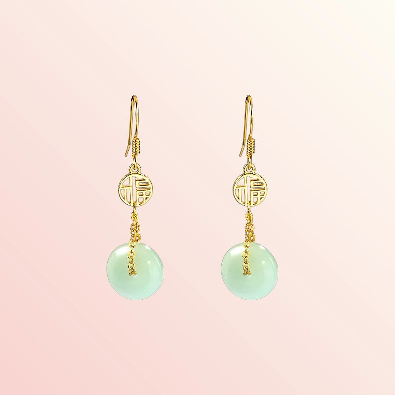 Gold earrings with green round jade on a pink background