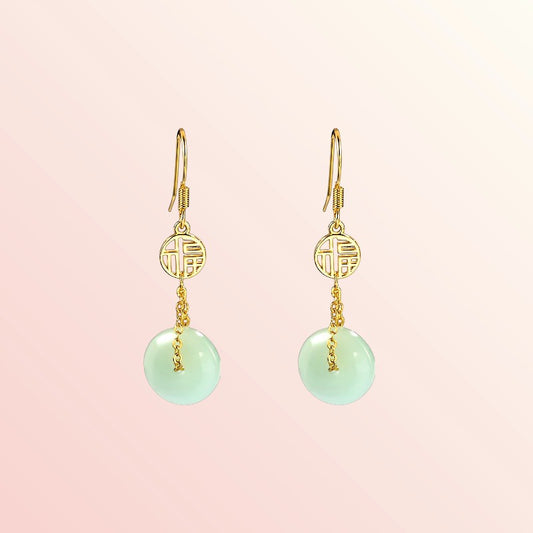 Gold earrings with green round jade on a pink background