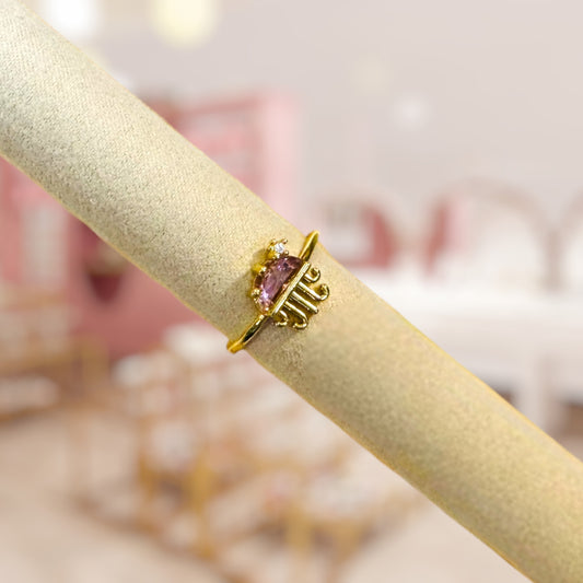 Gold jellyfish ring with a pink gemstone on a beige surface