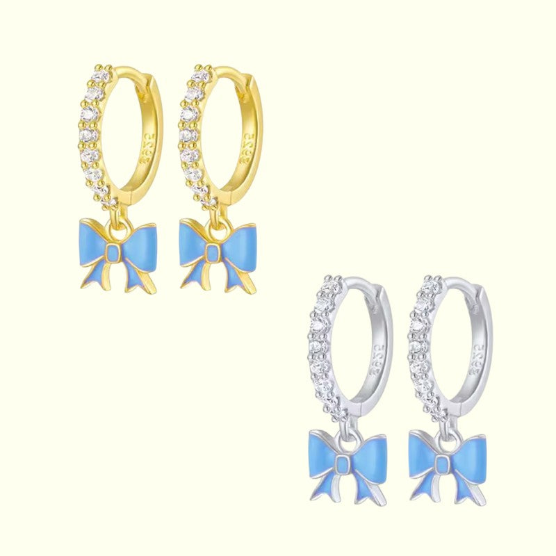 Pair of gold hoop earrings with blue bow charms on a white background