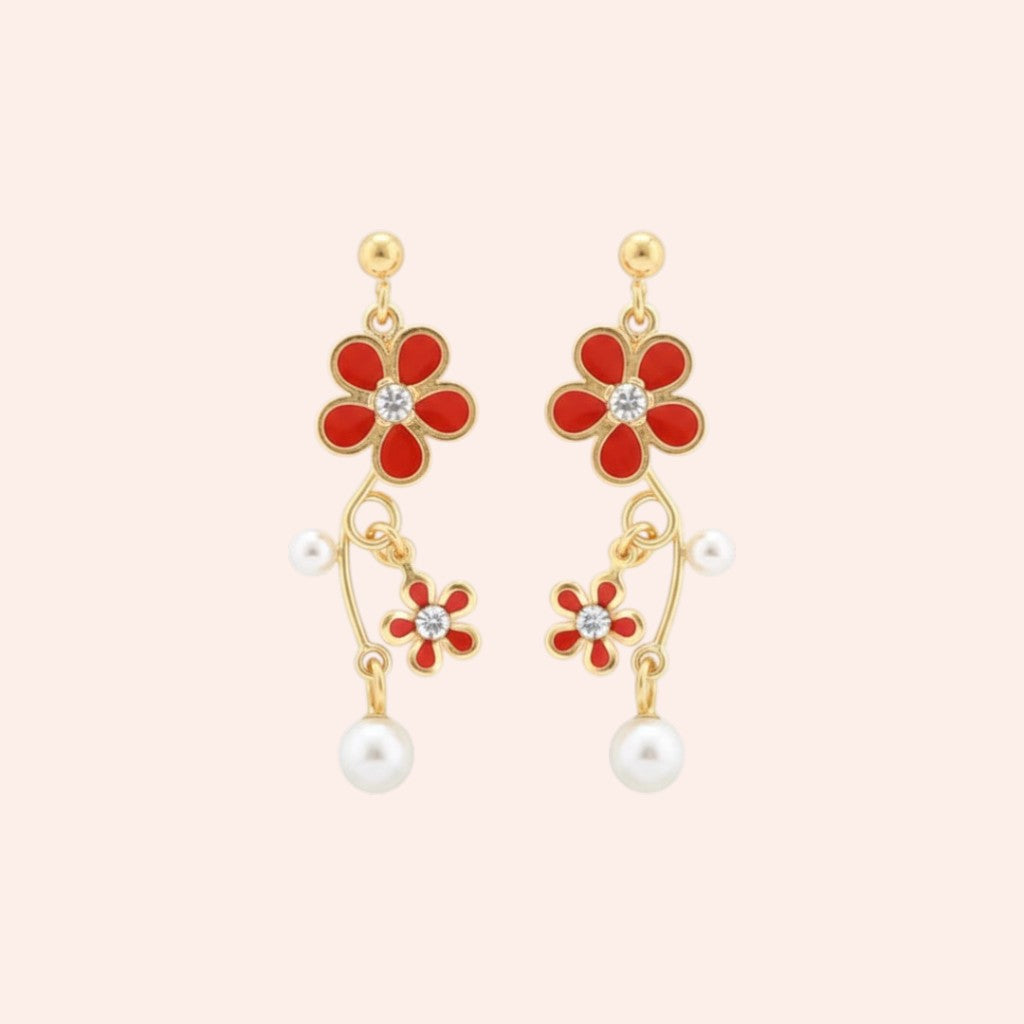 Gold earrings with red flower-shaped drops and pearl accents on a light pink background