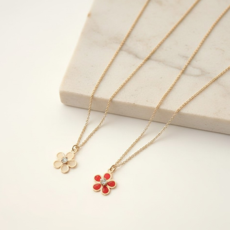 Two gold necklaces with flower pendants on a light surface