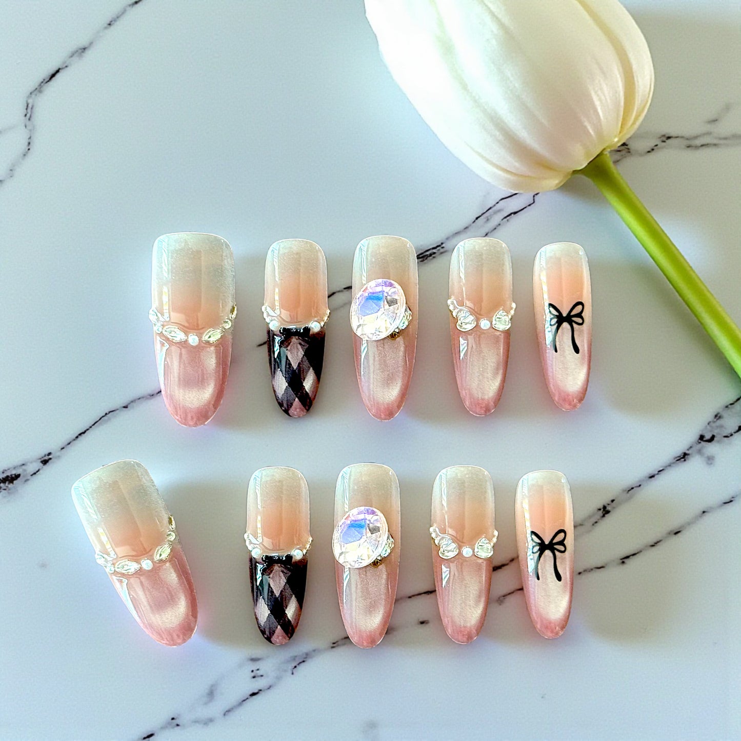 Decorative false nails with various designs on a marble surface with a tulip.