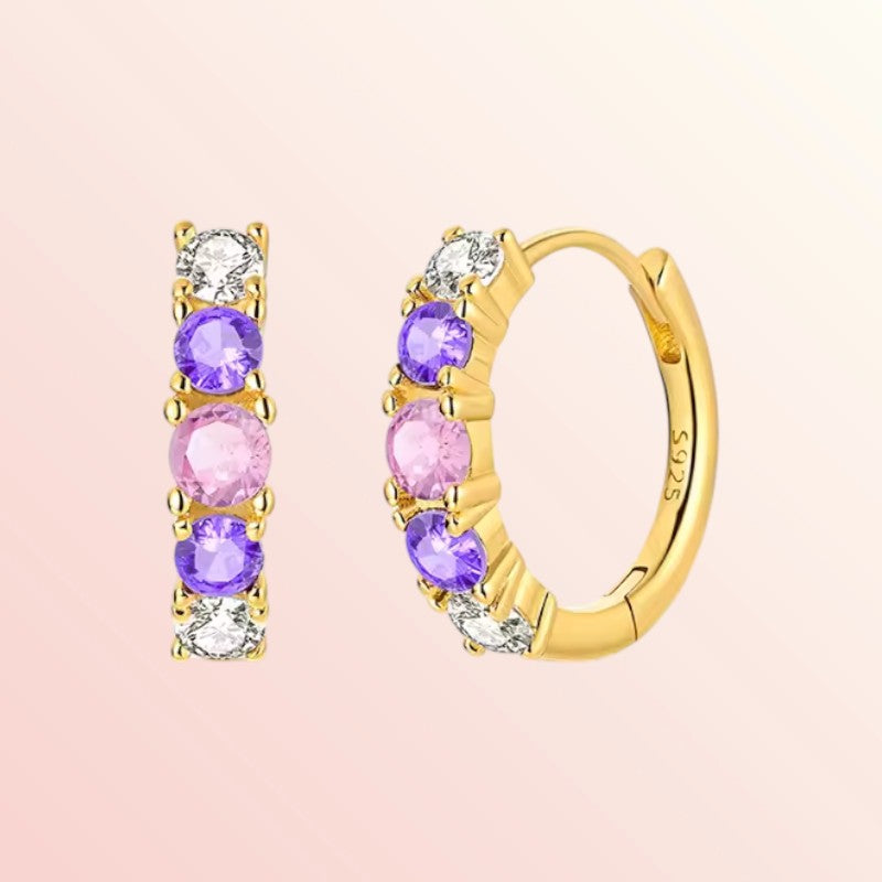 Gold hoop earrings with colorful gemstones on a pink background