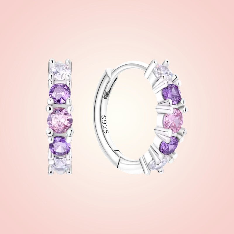 Silver hoop earrings with pink gemstones on a pink background