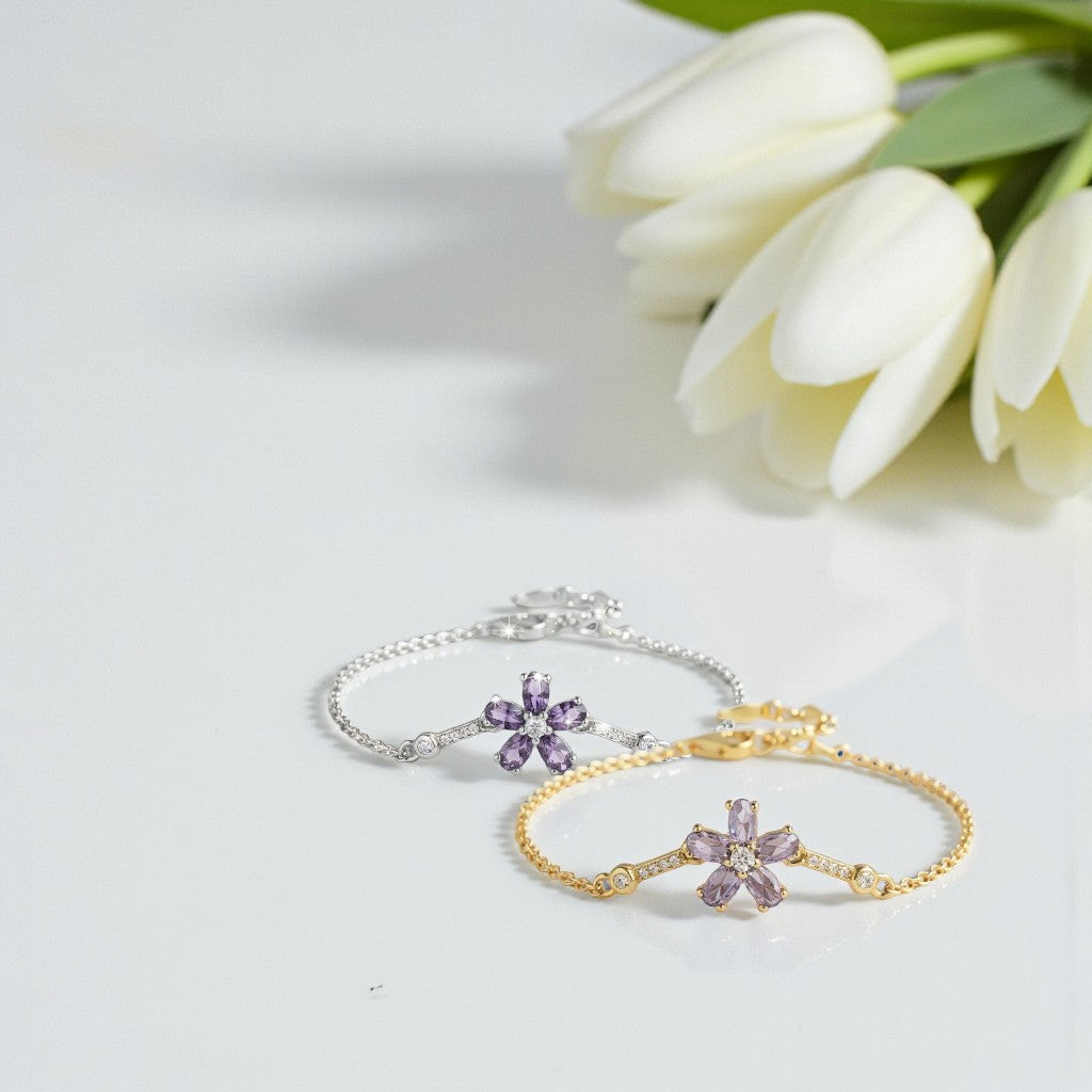 Two floral-themed bracelets, one gold and one silver, with purple stones on a white surface with tulips.