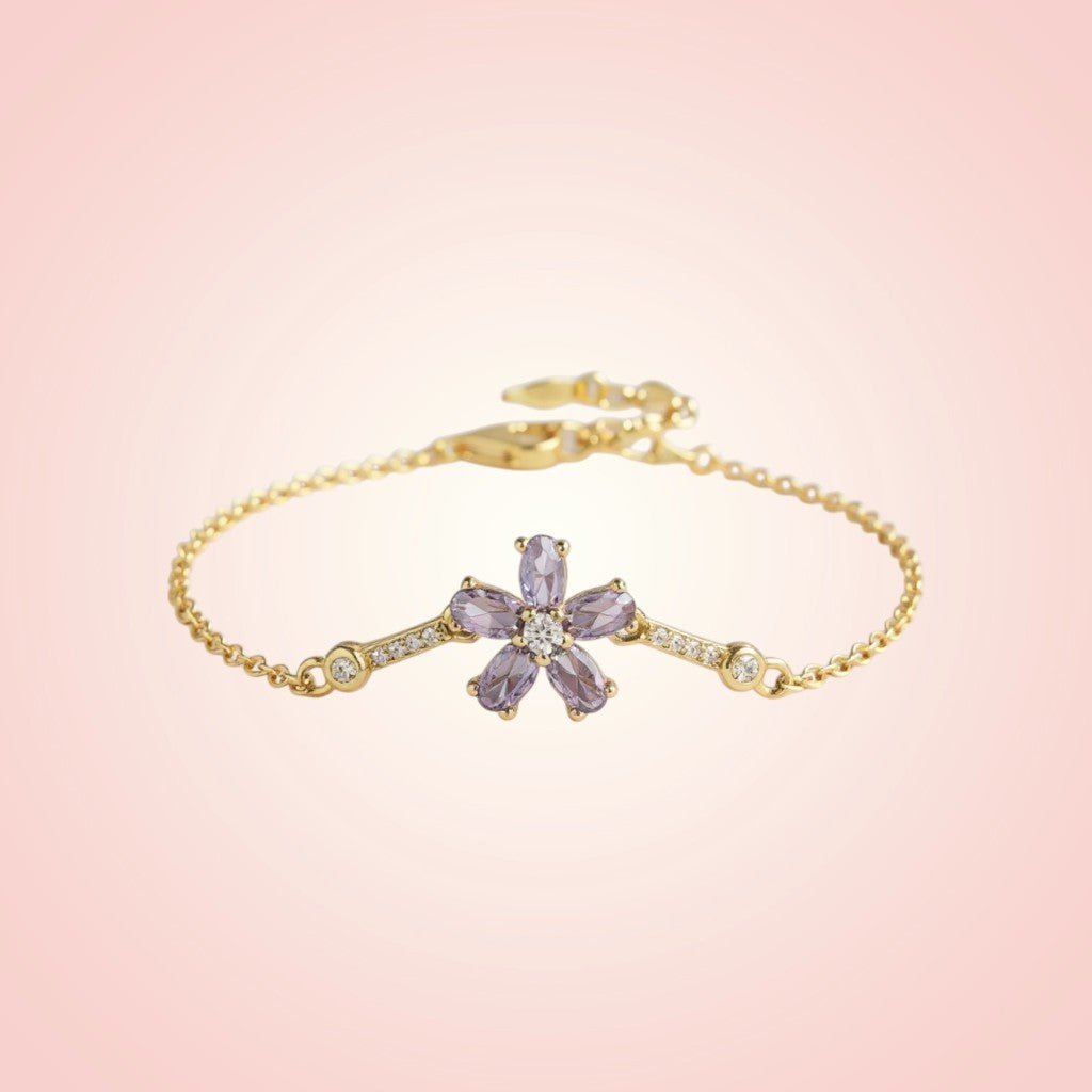 Gold bracelet with a purple flower-shaped clasp on a pink background