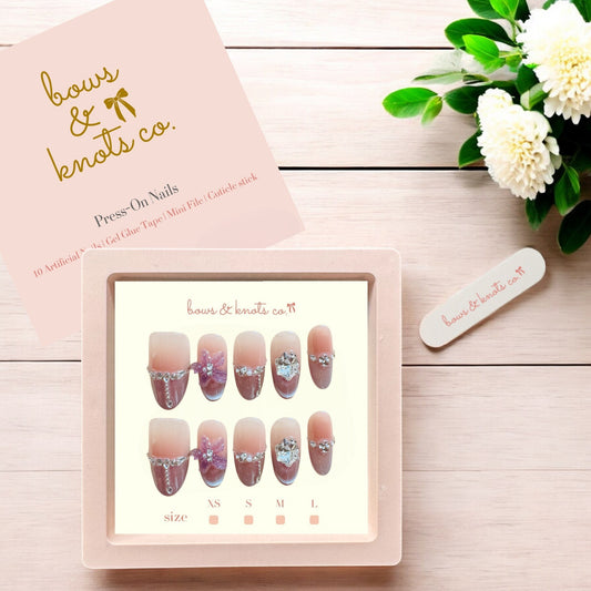 Nail art display with 'bows & knots co.' branding on a wooden surface with flowers.