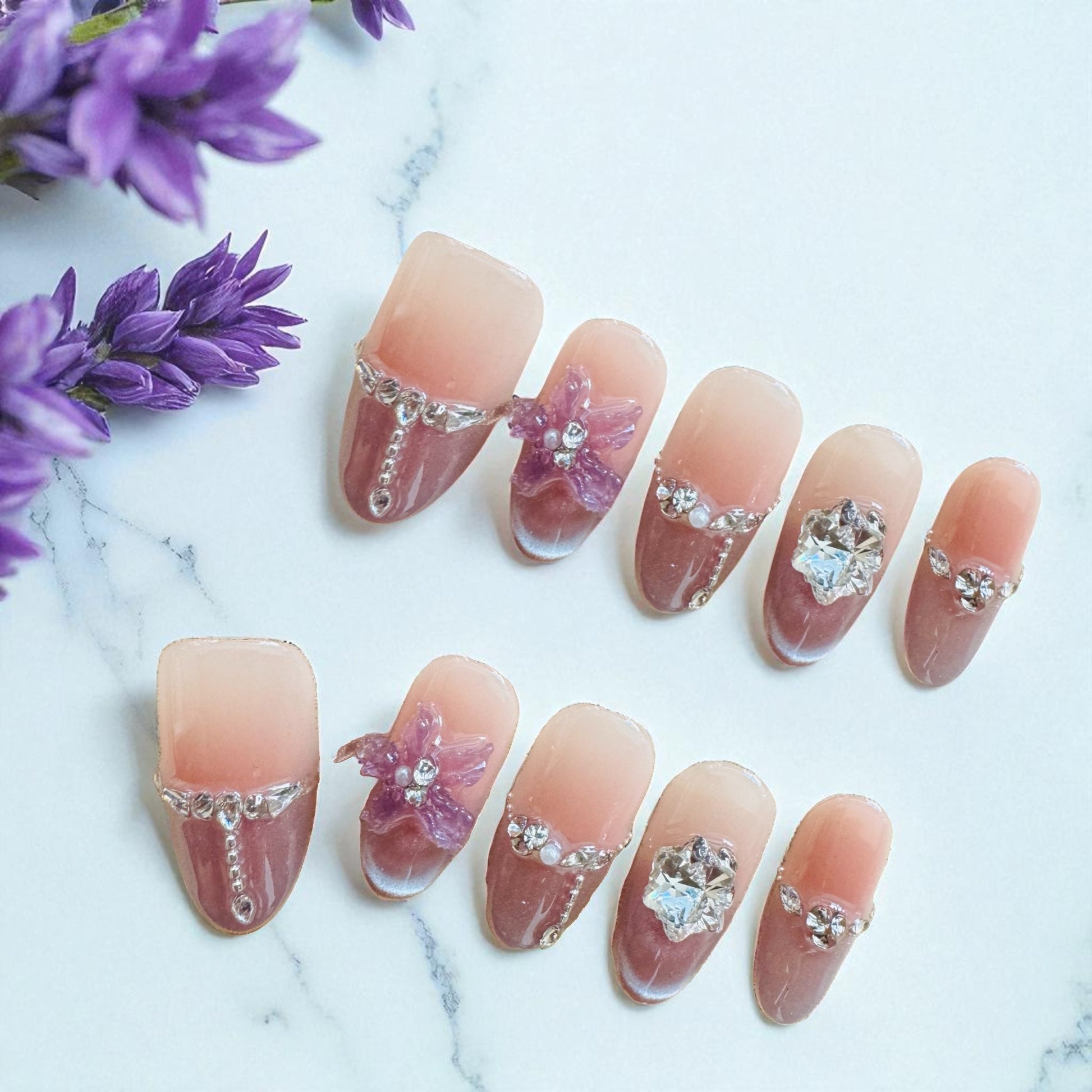 Nails with floral and gemstone decorations on a marble surface with purple flowers.
