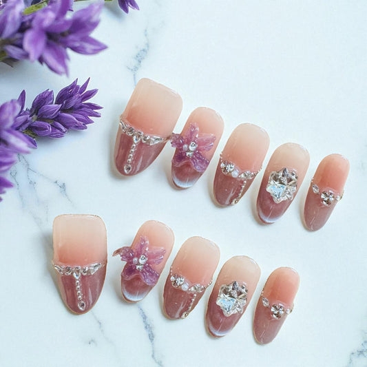 Nails with floral and gemstone decorations on a marble surface with purple flowers.