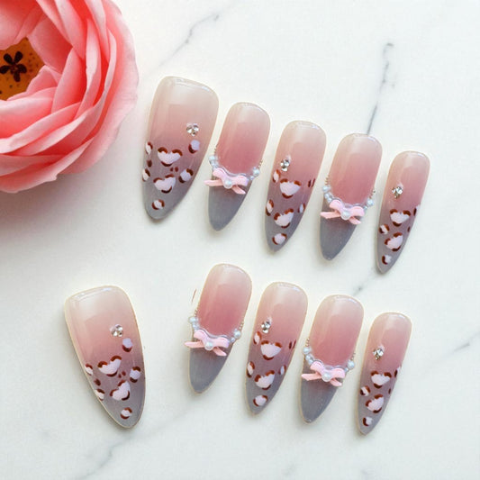 Decorative nails with pink and gray design on a white surface with a pink rose.
