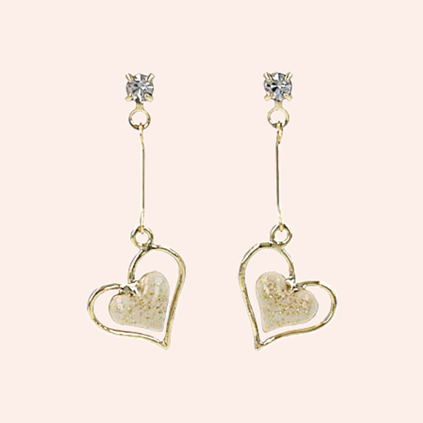 Heart-shaped earrings with gold frame and clear gemstones on a light pink background