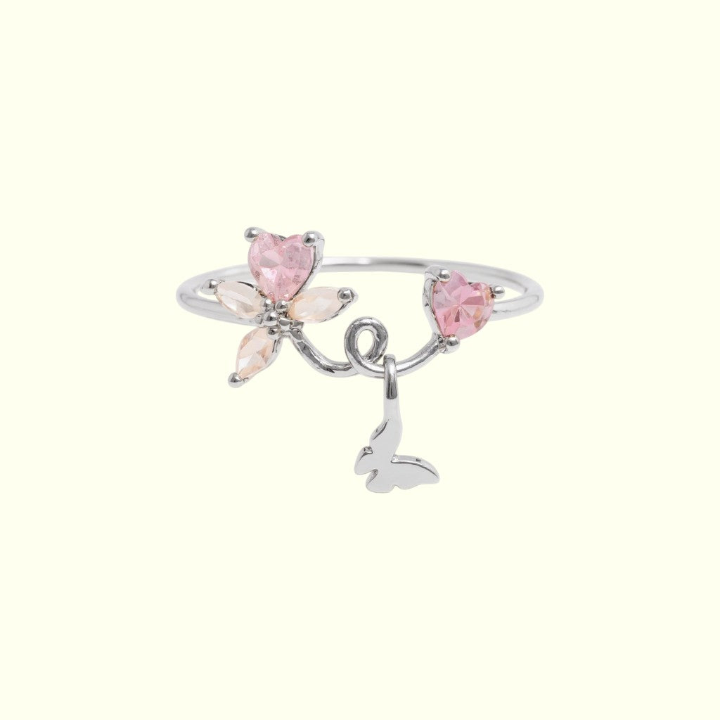 Silver ring with pink heart-shaped stones and butterfly charms on a white background