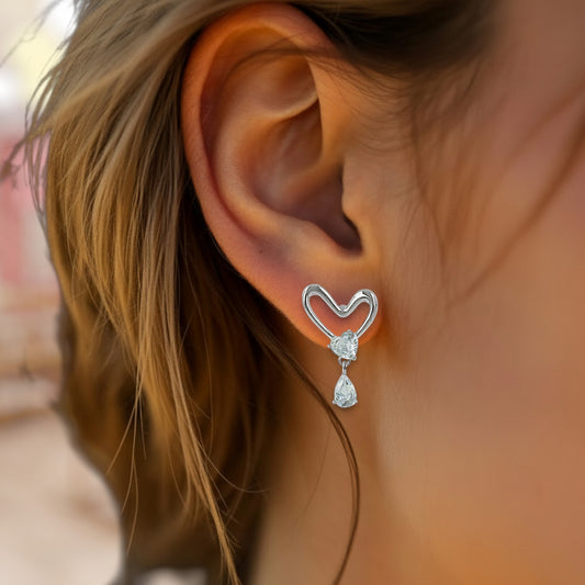 Silver heart-shaped earring with a dangling gemstone worn by a person.