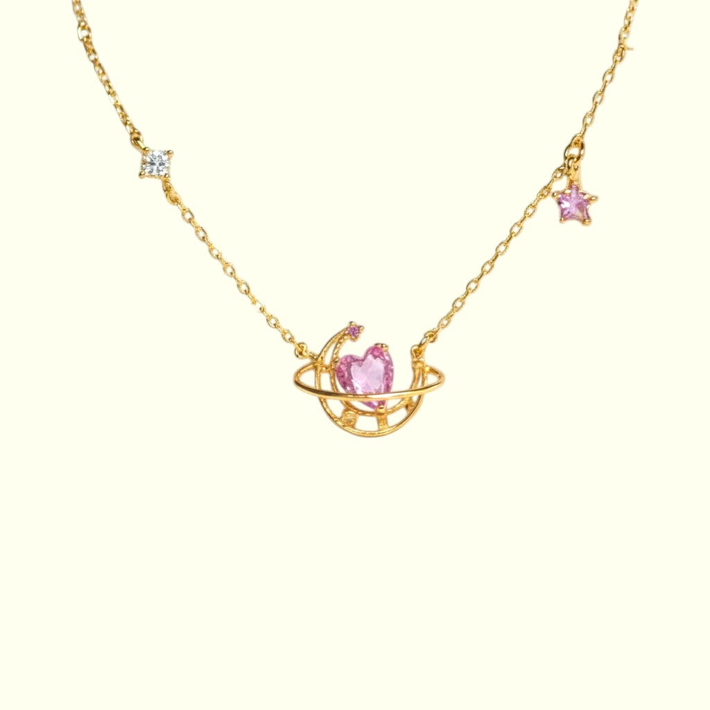 Gold necklace with a pink heart pendant on a white background