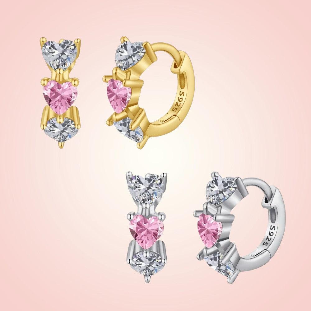 Gold and silver hoop earrings with pink heart-shaped stones on a pink background